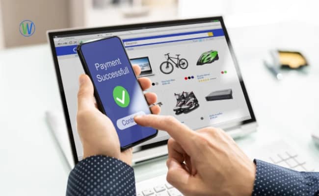 A person completes an online transaction. The laptop displays an online shopping site, while the phone confirms "Payment Successfull".