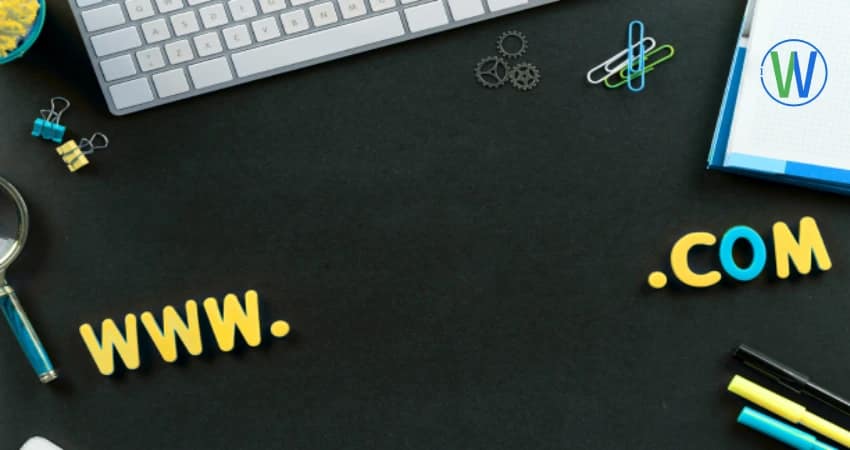 A black desk features a keyboard and the words "www .com" in colorful letters. A WordPress logo sits on a white pad, adding a touch of design flair.
